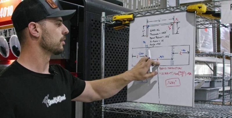 Screenshot of the Video Guide with Jake in front of a white board showing where dimensions are removed from the laser cut part after calculating the bend deduction.